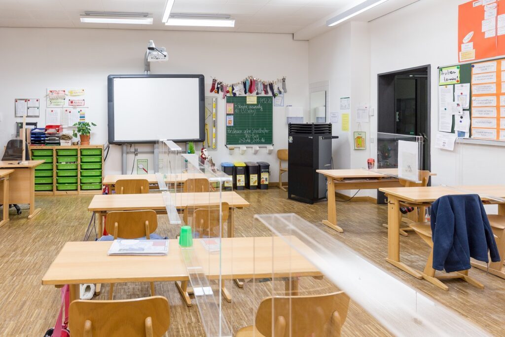 Schulklasse ausgestattet mit TAC V+ Hochleistungsluftreiniger und Acrylglas-Trennwänden mit umlaufender Aerosol-Schutzkante.